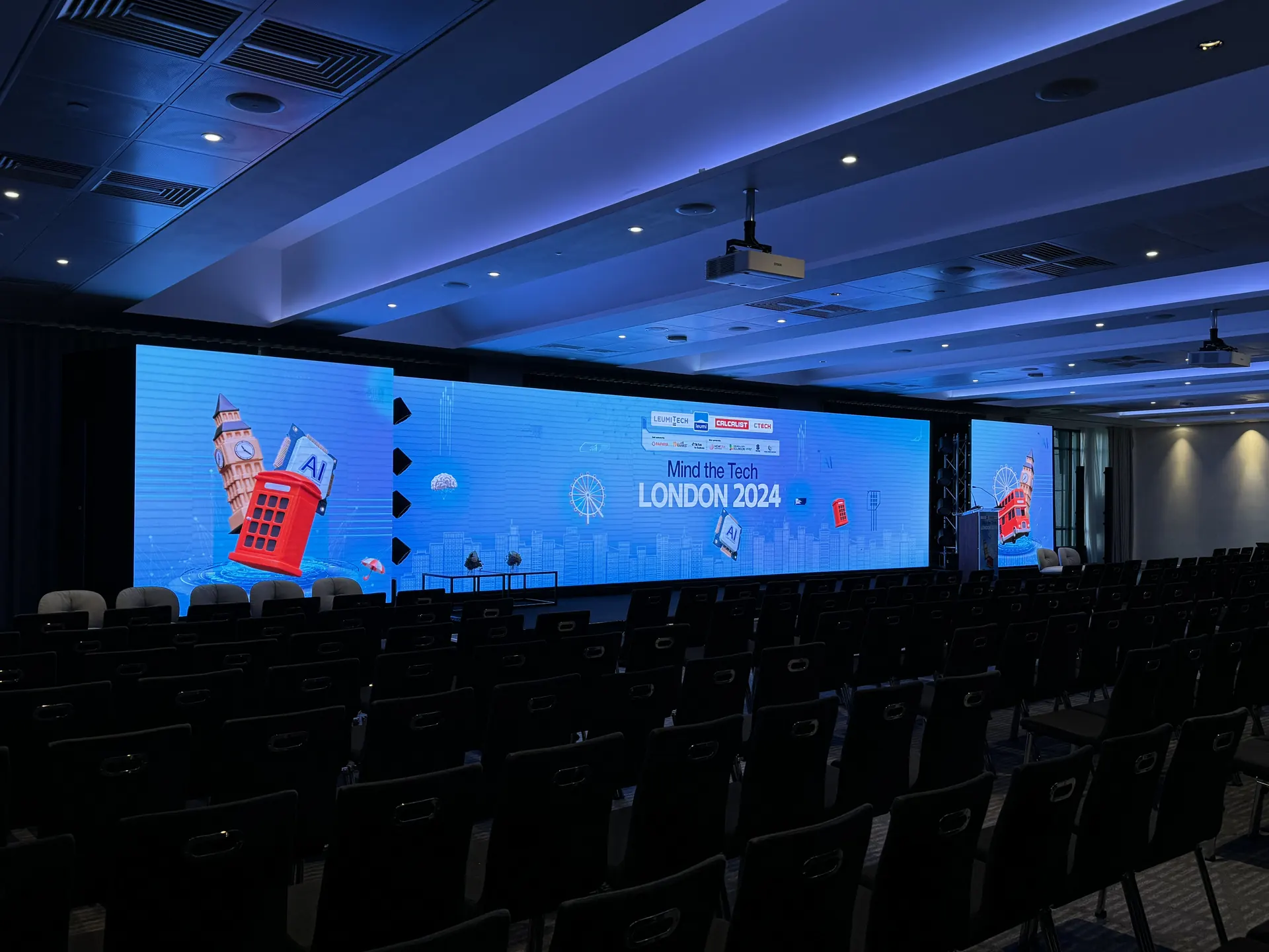 Konferenciaterem előkészítve: a terem teljes szélességében LED fal, előtte üres széksorok, oldalt pulpitus.